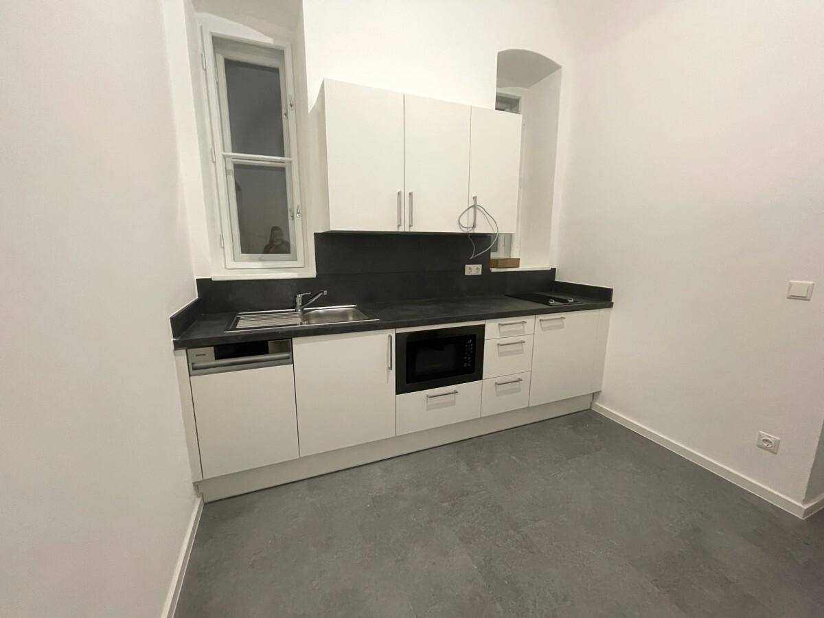 Moderne Küchenzeile mit weißen Schränken, dunkler Arbeitsplatte, integrierten Geräten und Fenster.