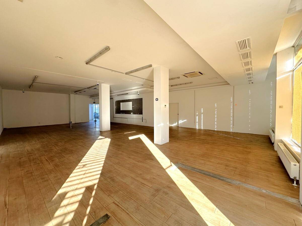 Weitläufiger Geschäftsraum mit Holzboden, weißen Wänden und Deckenleuchten, durchflutet von Sonnenlicht.