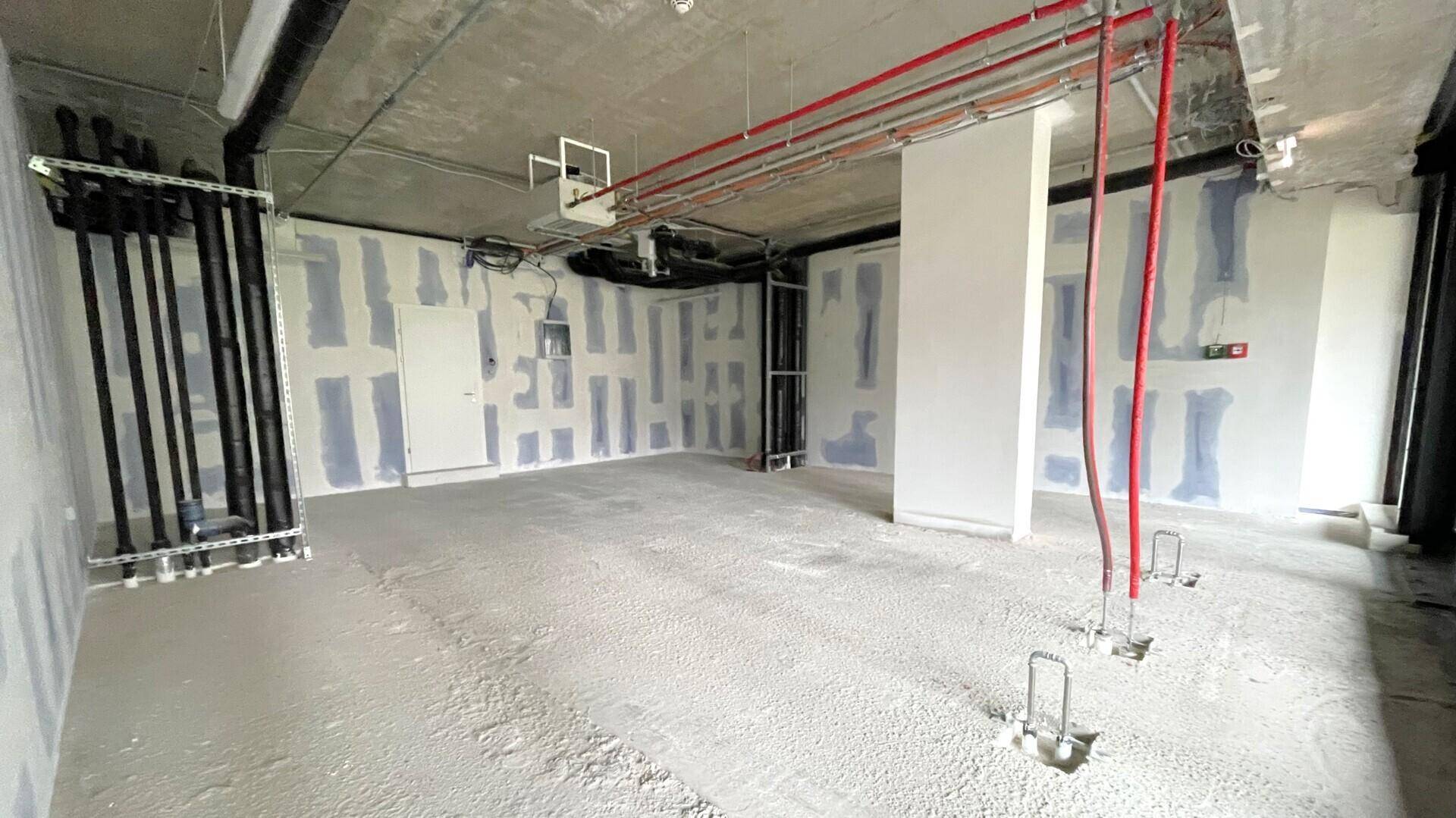 Weitläufiger Gewerberaum im Rohbauzustand mit freiliegenden Deckeninstallationen und unfertigen Wänden, bereit für den Ausbau.