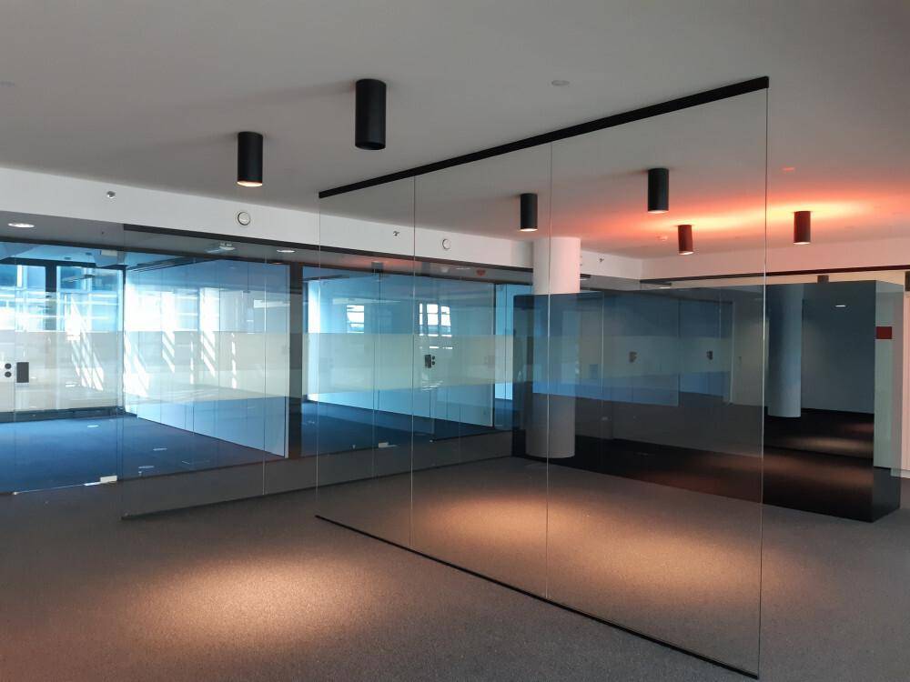 Moderner Bürobereich mit Glaswänden, dunklem Teppichboden und stilvoller Beleuchtung.