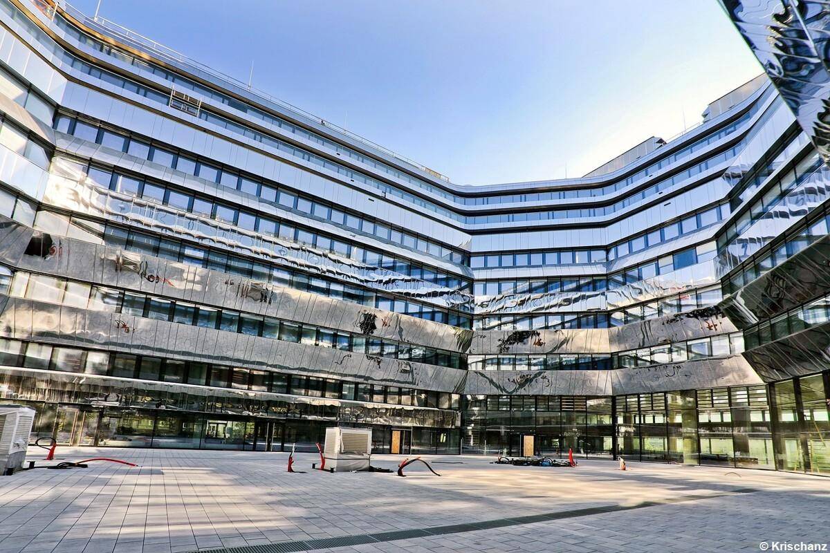 Weitläufiger Innenhof eines modernen Gebäudes mit reflektierenden Glasfassaden und klaren Linien.