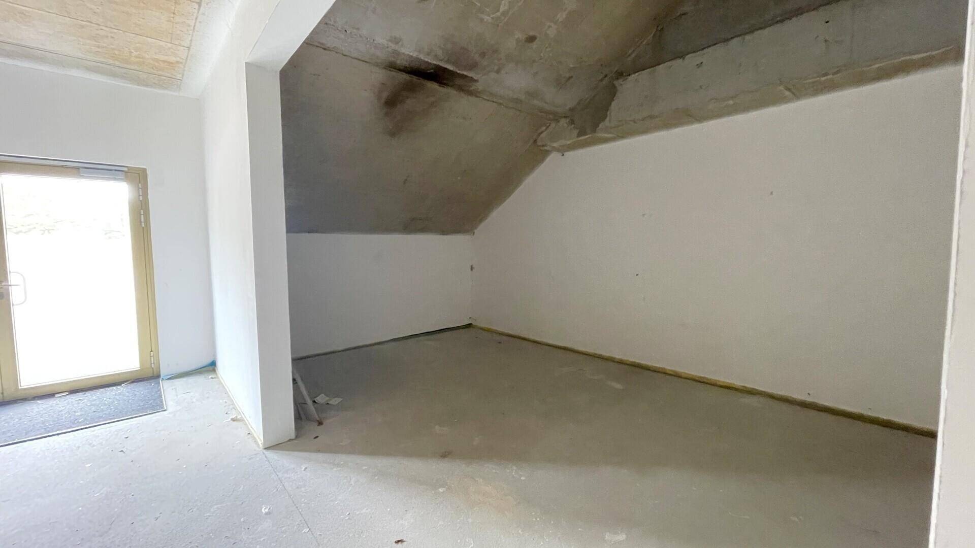 Unfertiger Raum mit schräger Decke und Betonboden, der auf einen Dachboden oder eine Abstellkammer hindeutet.