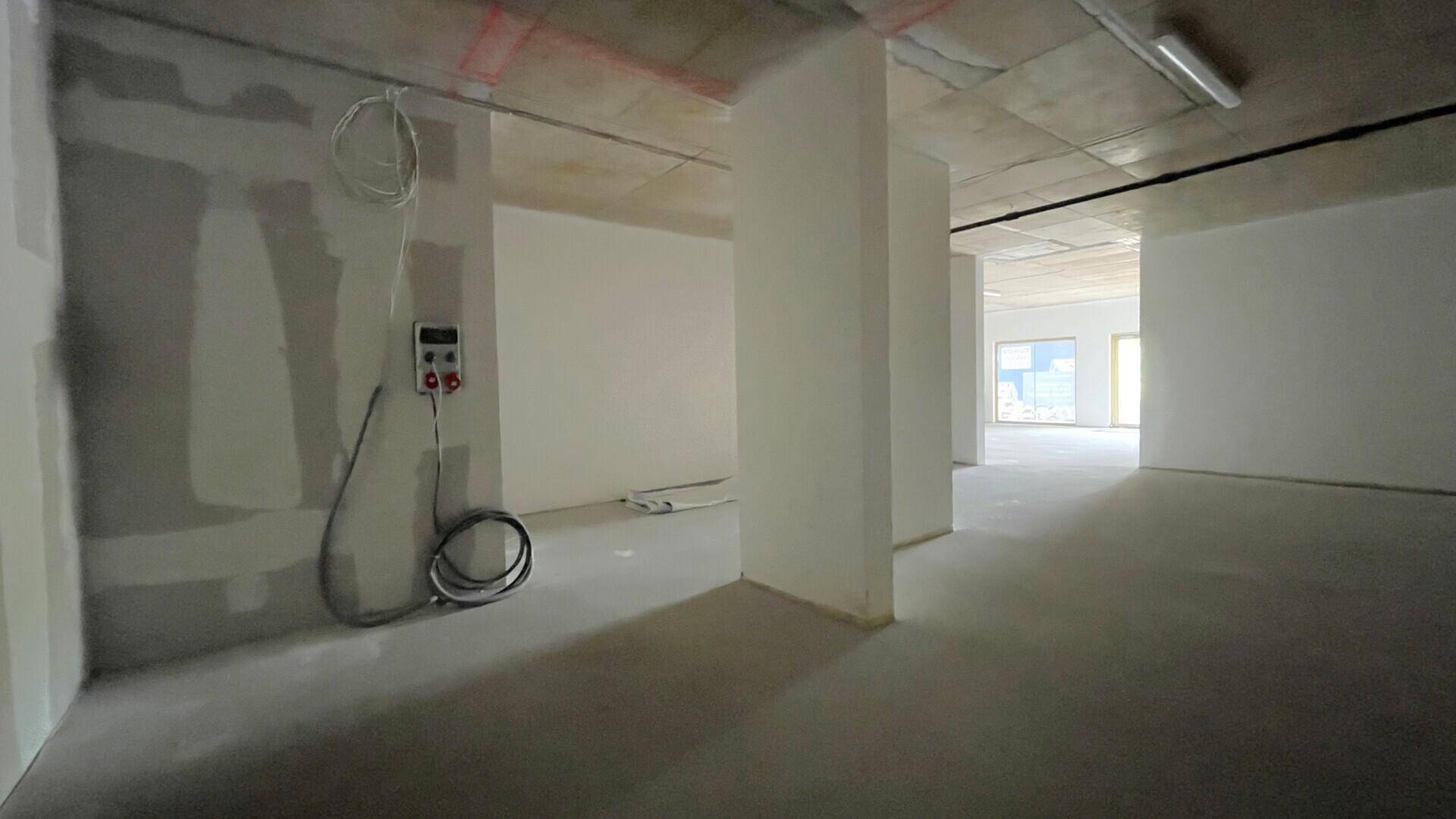 Unfertiger Innenraum mit sichtbaren elektrischen Installationen, Betonboden und -decke sowie Fenstern im Hintergrund.