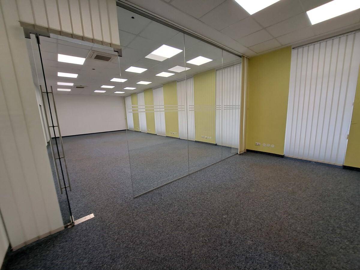 Geräumiger Bürobereich mit Teppichboden, Glaswand und vertikalen Jalousien an den Fenstern, gut beleuchtet.