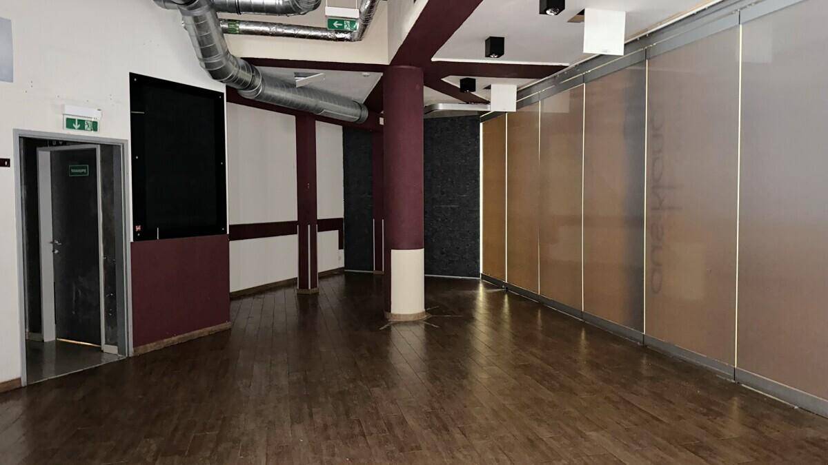 Großer leerer Geschäftsraum mit Holzboden, Säulen und sichtbaren Lüftungsrohren an der Decke.