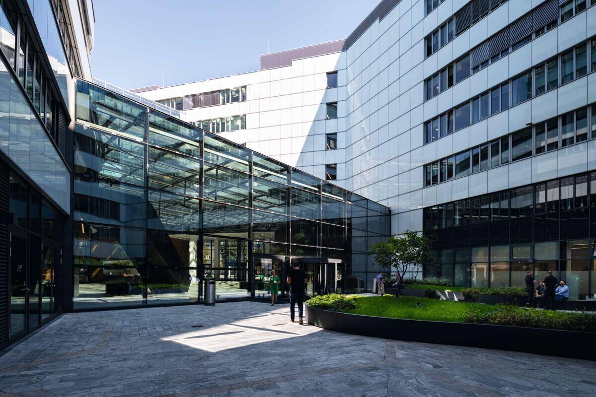 Moderner Innenhof mit Glasbrücken, Grünflächen und Sitzgelegenheiten zwischen Bürogebäuden.