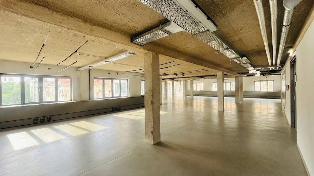 Geräumiger Gewerberaum mit viel Tageslicht, Betonstruktur und freiliegenden Deckeninstallationen für industrielle Ästhetik.