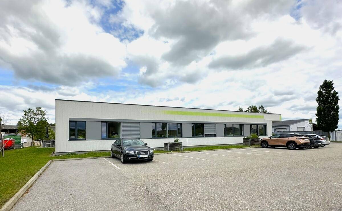 Seitenansicht eines modernen Bürogebäudes mit großen Fenstern und einem geräumigen Parkplatz davor.