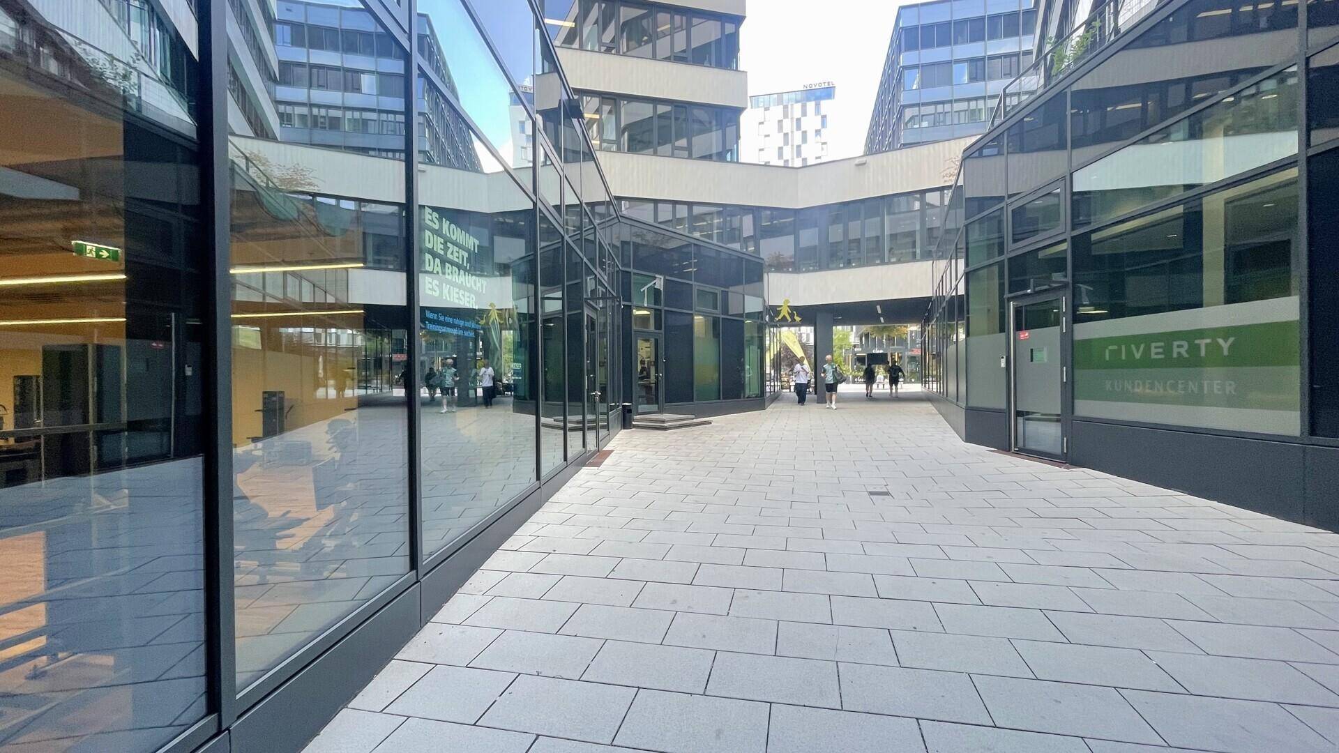 Moderner Außenbereich zwischen Geschäftsgebäuden mit Glasfassaden und gepflastertem Weg.
