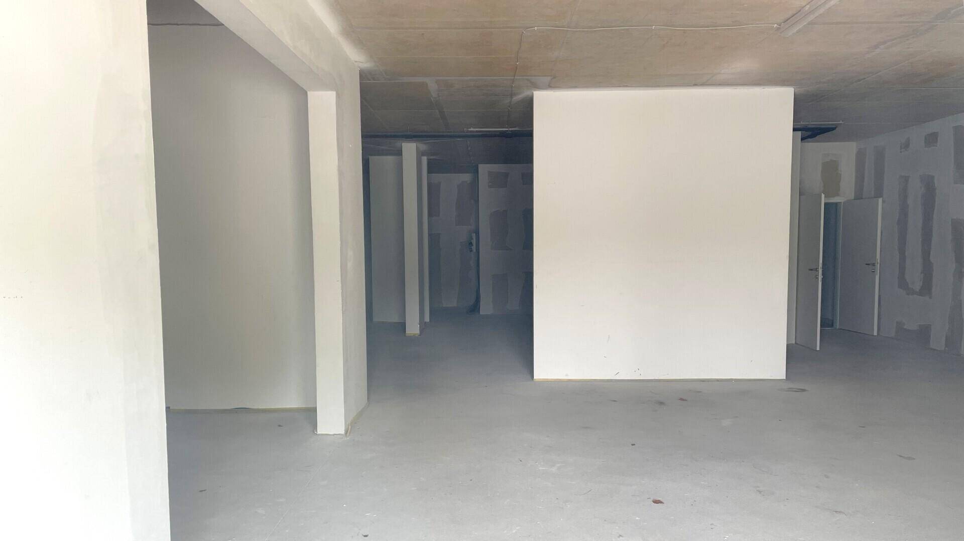 Großer, unfertiger Innenraum eines Geschäfts mit weißen Wänden und Betonboden, bereit für den Ausbau.