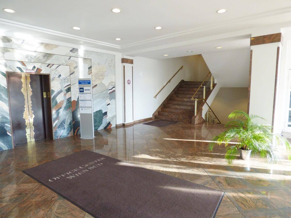 Geräumige Lobby mit glänzendem Marmorboden, Treppe und Aufzug, hell erleuchtet durch Tageslicht.