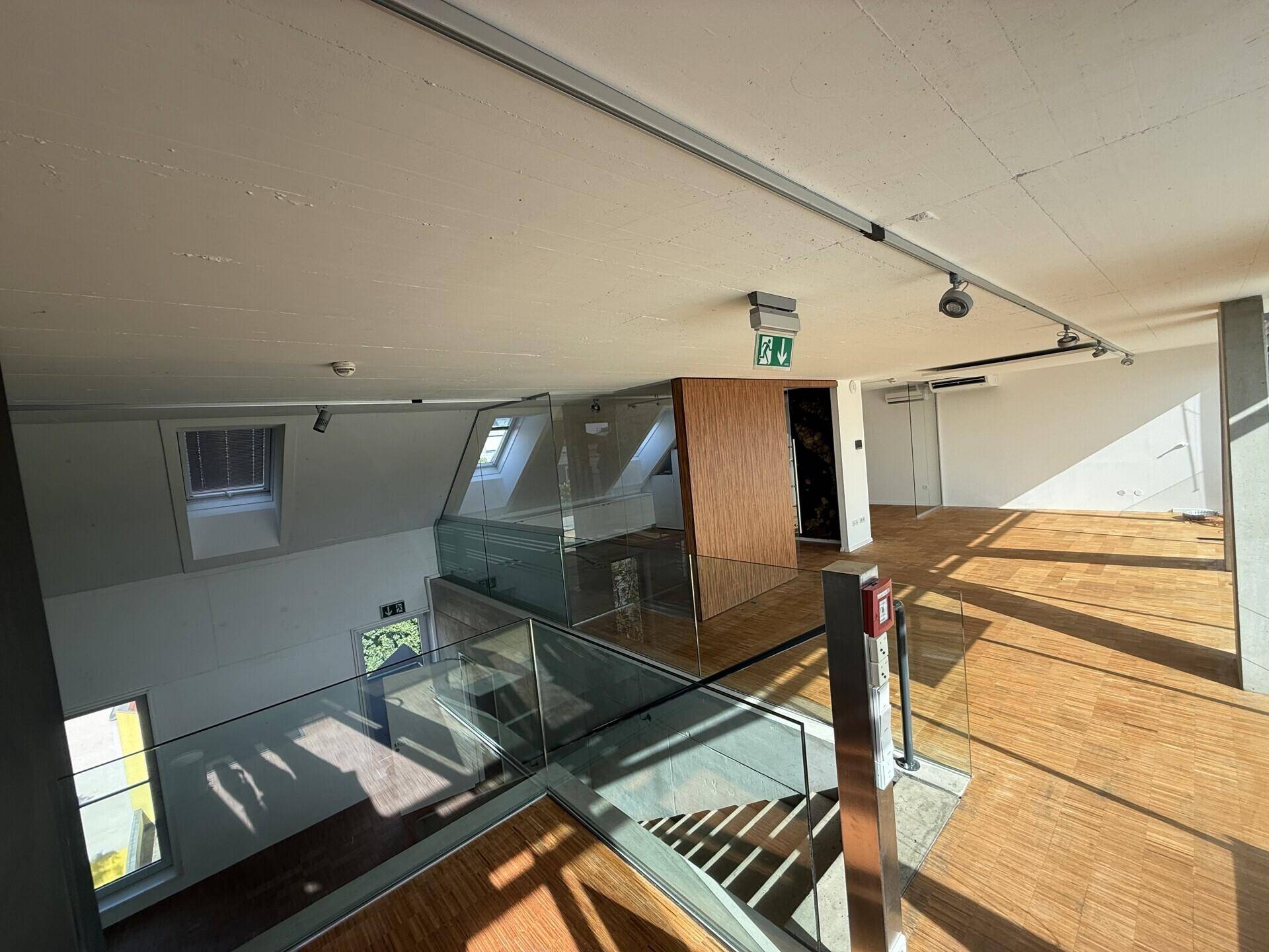 Offener Bürobereich mit Holzboden, Glasgeländer und Blick auf die darunterliegende Etage.