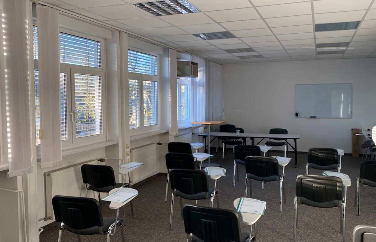 Schulungs- oder Konferenzraum mit vielen Stühlen, Tischen und einer Whiteboard-Wand für Präsentationen.