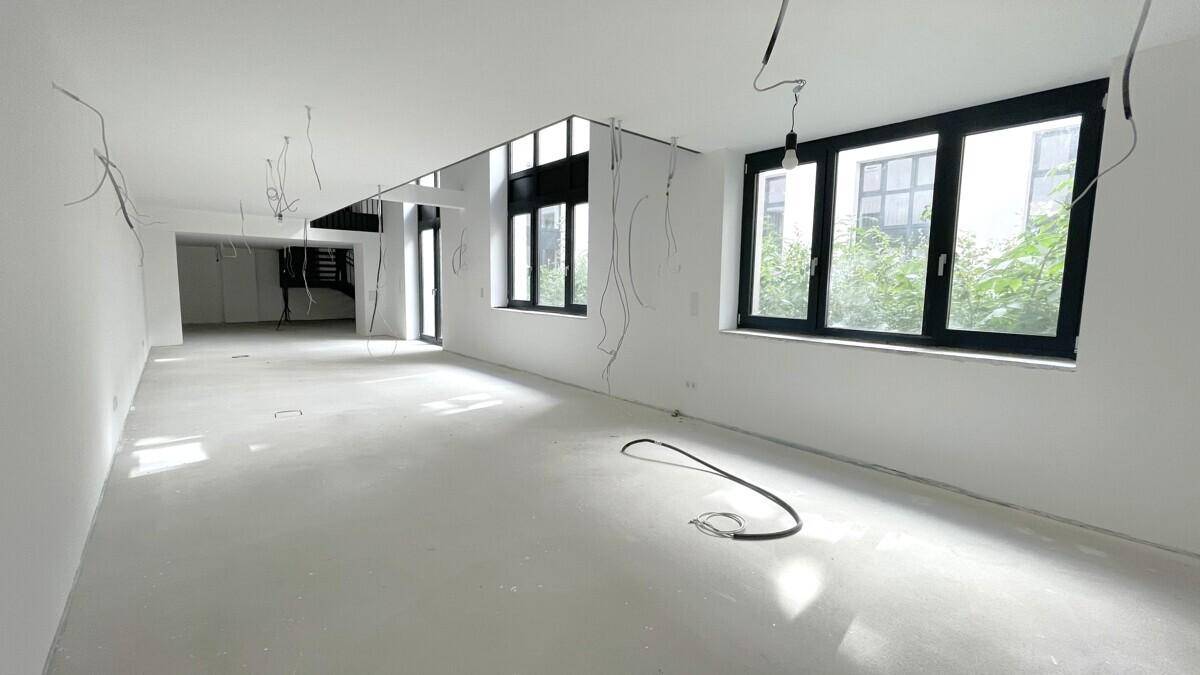Großer, heller Raum mit vielen Fenstern, Betonboden und sichtbaren Kabeln für die Installation.