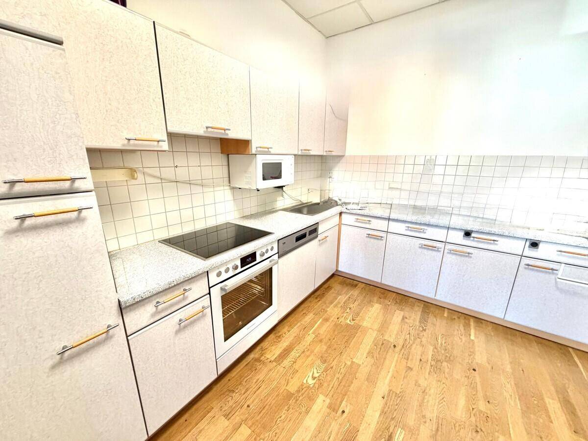 Funktionale Küche mit weißen Schränken, heller Arbeitsplatte, Fliesenrückwand und Holzboden.