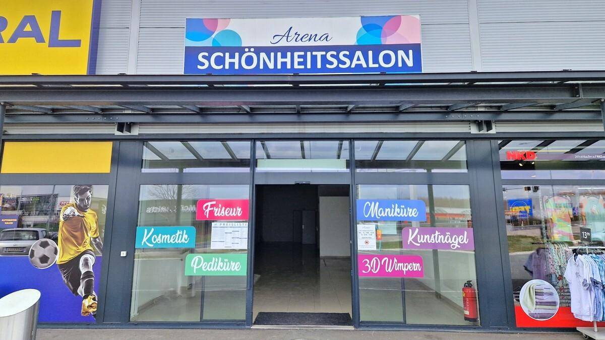 Nahaufnahme des Eingangs eines Schönheitssalons mit Schiebetüren und Werbeaufklebern für Dienstleistungen.