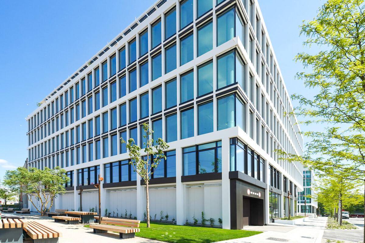 Ansicht eines modernen Bürogebäudes mit großen Glasflächen und Sitzgelegenheiten im Außenbereich.