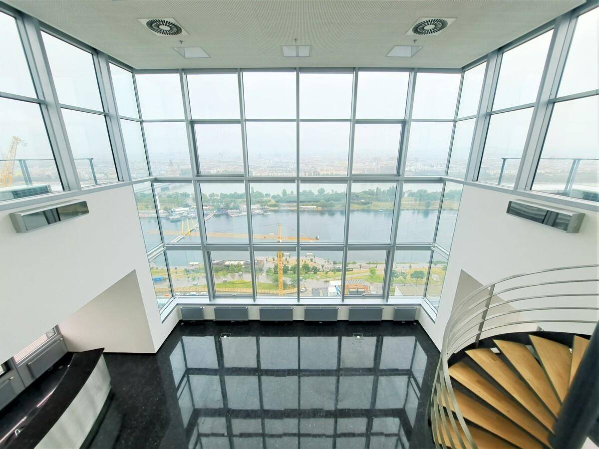Großer, heller Raum mit raumhohen Fenstern, die einen weiten Blick auf den Fluss bieten, und einer eleganten Wendeltreppe.