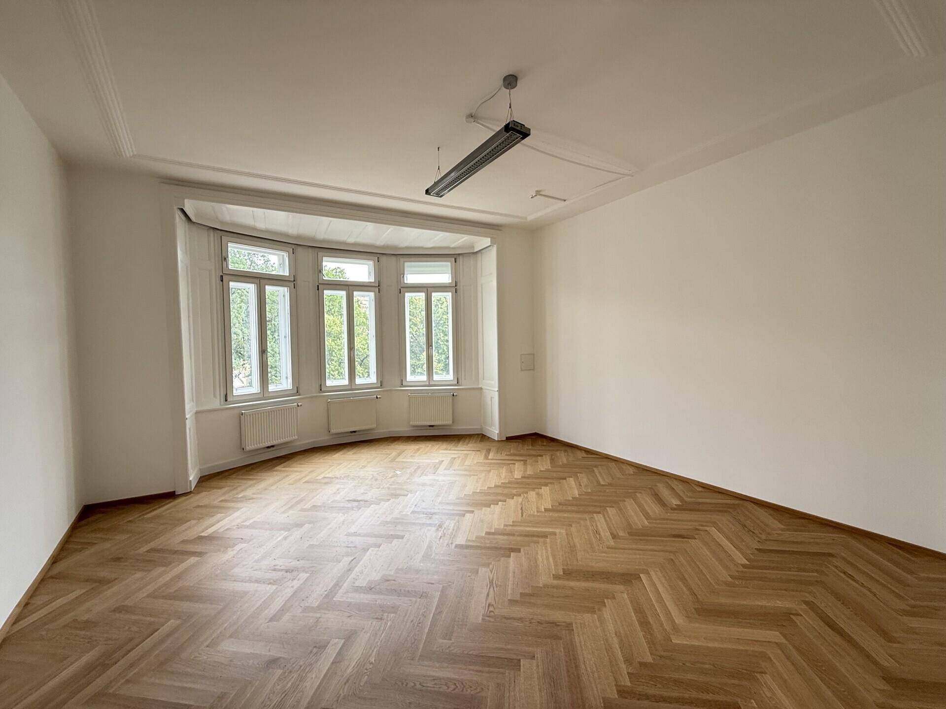 Helles Büro mit Erkerfenstern, Fischgrätparkett und einer minimalistischen Deckenleuchte, mit Stadtblick.