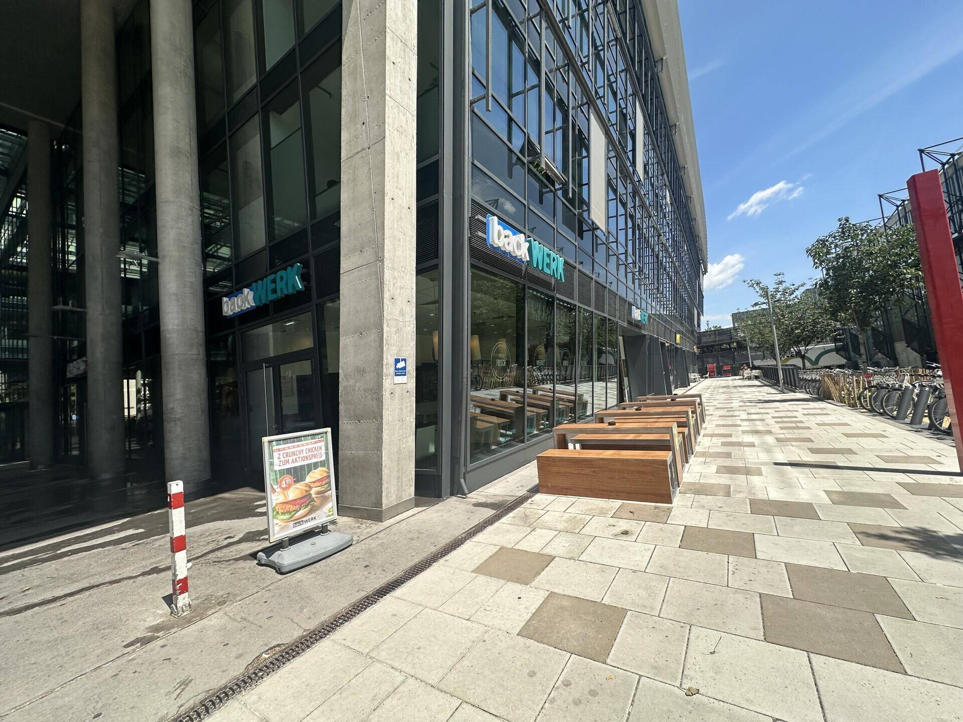 Ansicht der modernen Geschäftsfassade mit großen Glasflächen und Sitzgelegenheiten im Außenbereich.