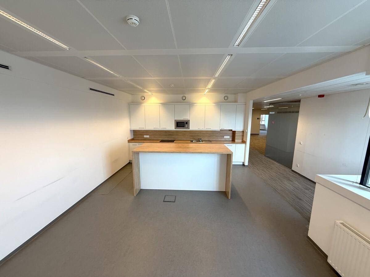 Moderne Teeküche in einem Bürobereich mit weißen Schränken, Holzarbeitsplatte und Mikrowelle.