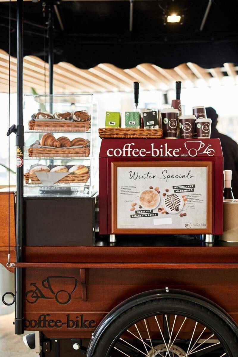 Mobiler Kaffeestand mit Gebäck und Getränkeangeboten, bereit für den Verkauf in einem Innenbereich.