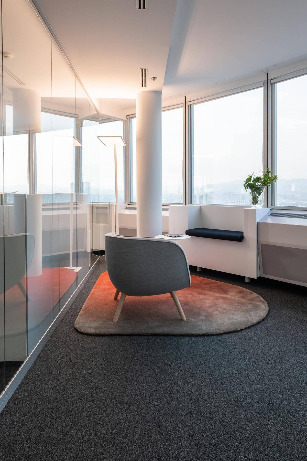 Gemütlicher Loungebereich mit Sessel, Teppich und großen Fenstern mit Stadtblick.