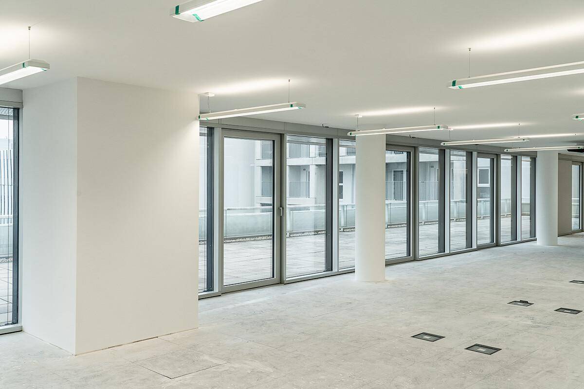 Heller Büroraum mit großen Glasfronten, die viel Tageslicht hereinlassen und Zugang zu einem Außenbereich bieten.