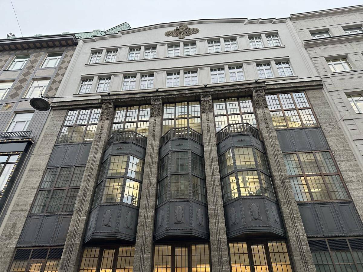 Detailansicht der historischen Gebäudefassade mit großen Fenstern und dekorativen Elementen, die das Licht reflektieren.