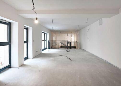 Erdgeschoss eines Gewerberaums mit hohen Fenstern und Blick auf die obere Galerie.