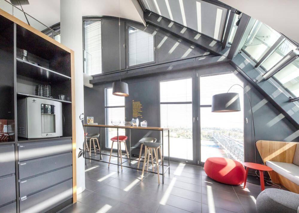 Moderner Loungebereich mit hohen Decken, großen Schrägfenstern, einer Bar und einem Getränkekühlschrank.