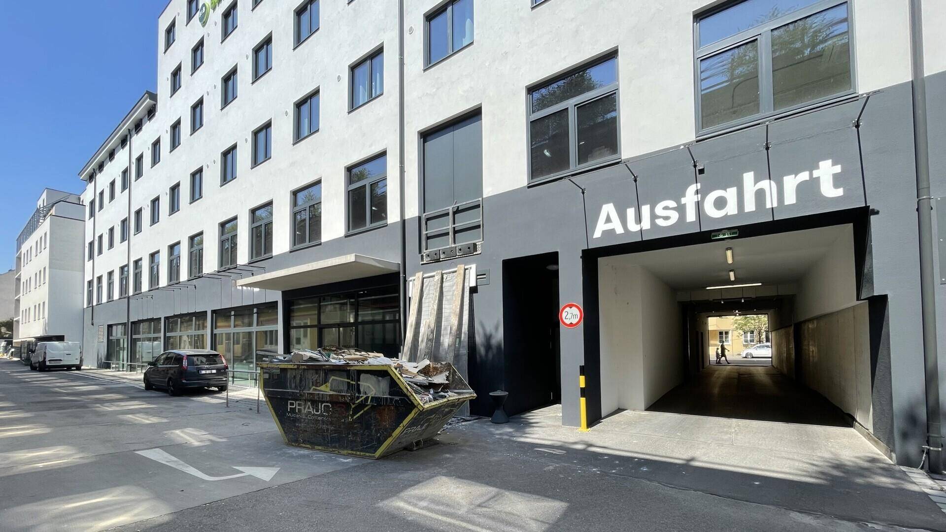 Ausfahrt einer Tiefgarage am Gebäude mit einem Bauschuttcontainer davor.