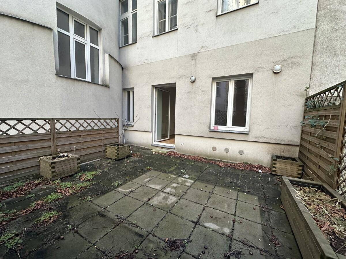 Kleiner Innenhof mit gepflastertem Bereich, Holzzäunen und Pflanzkübeln, umgeben von Gebäuden.