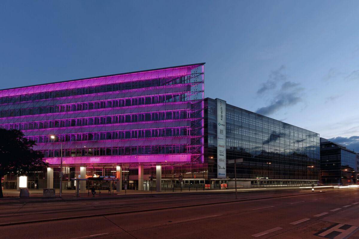 Modernes Bürogebäude mit auffälliger violetter Fassadenbeleuchtung und Glasfront bei Nacht.