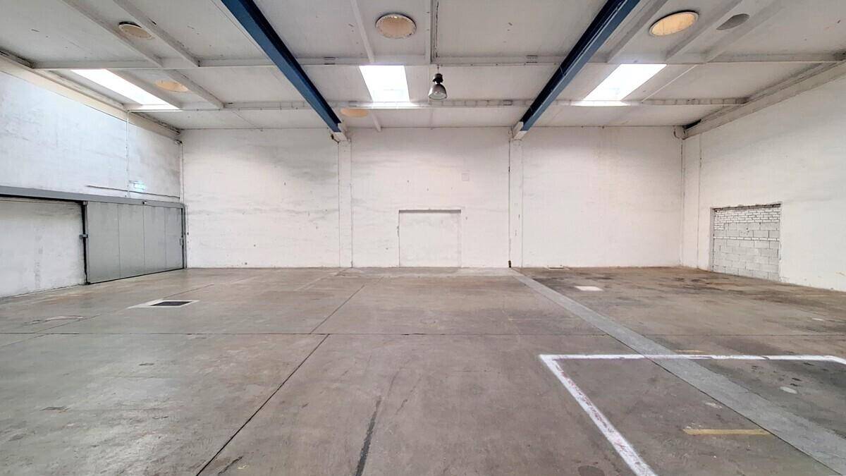 Geräumige Lagerhalle mit Betonboden, hohen Decken und einem großen Rolltor an der Seite.