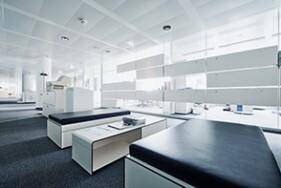 Moderner Loungebereich in einem Bürogebäude mit weißen Sitzbänken und dunklen Polstern.