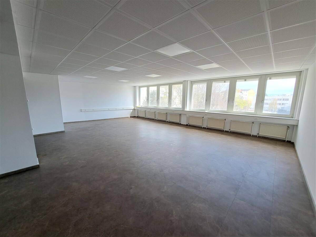 Geräumiger Büroraum mit vielen Fenstern, die viel Tageslicht hereinlassen, und dunklem Bodenbelag.