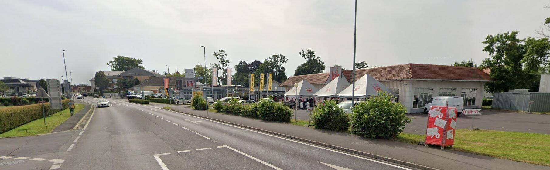 Weitwinkelansicht einer Geschäftsstraße mit einem KiK-Laden, Parkplätzen und weiteren Geschäften im Hintergrund.