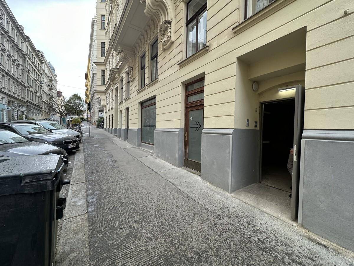 Eingangsbereich eines Altbaus an einer Straße mit parkenden Autos und klassischer Architektur.