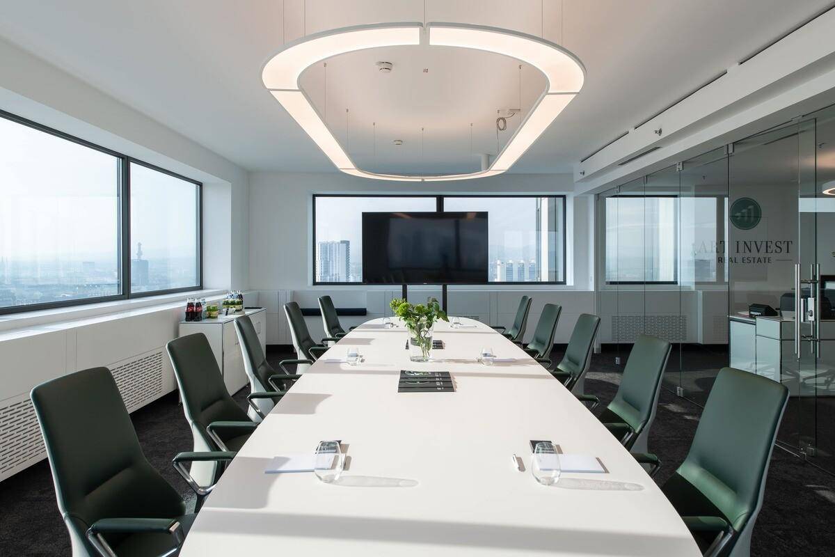 Großer Konferenzraum mit ovalem Tisch, bequemen Stühlen und einem Bildschirm an der Wand.