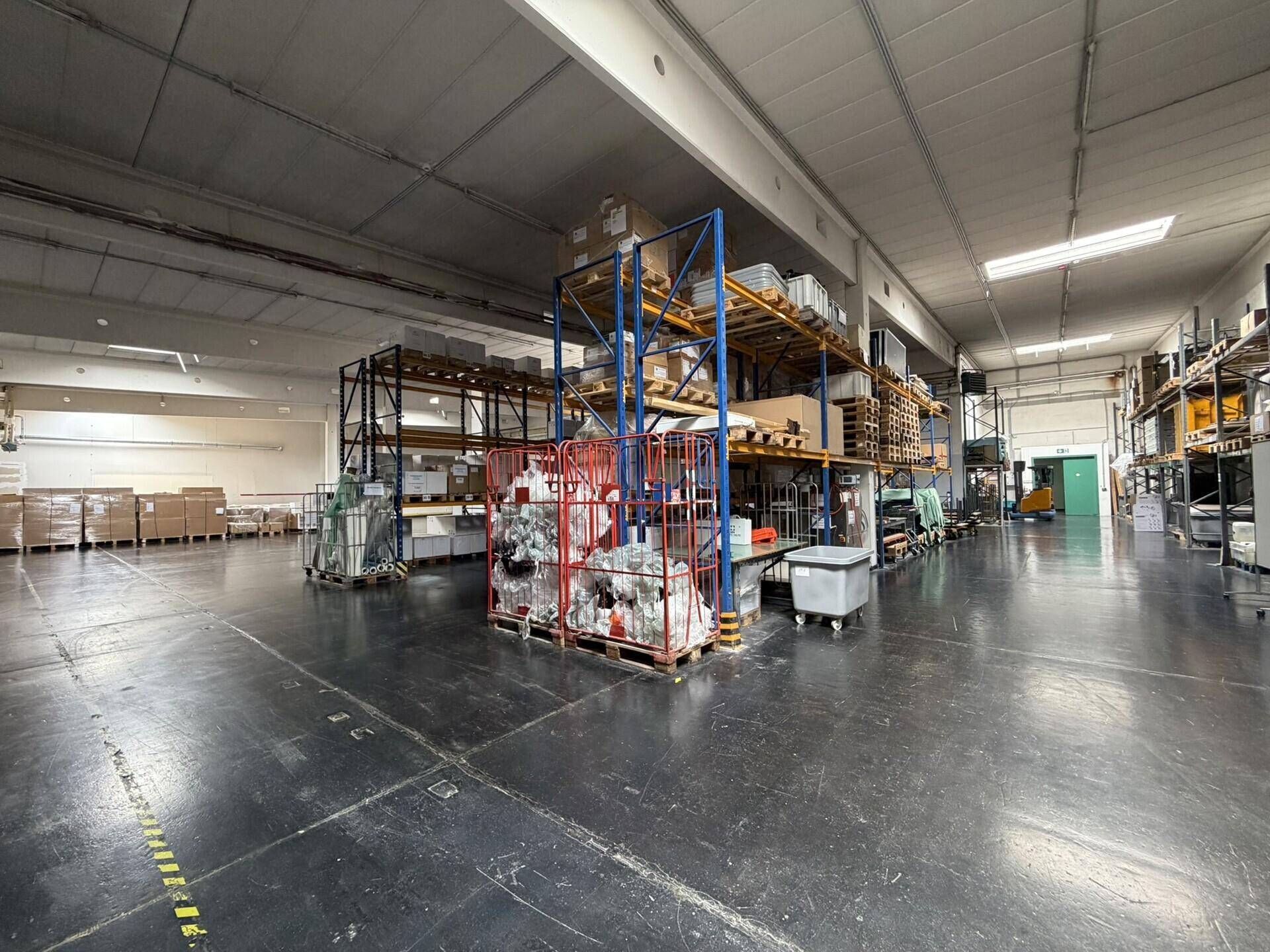 Geräumige Lagerhalle mit hohen Regalen, Waren und einem Gabelstapler im Hintergrund.
