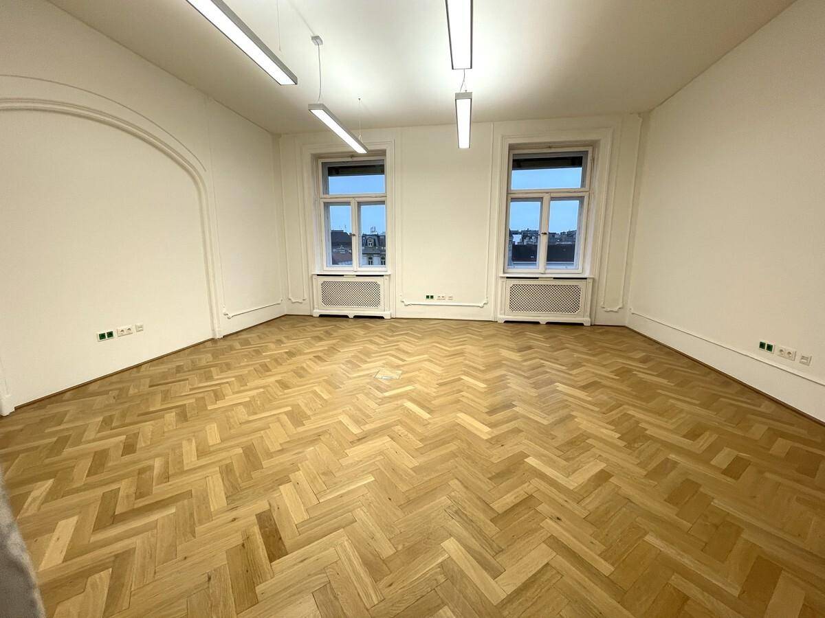 Heller Büroraum mit Fischgrätparkett, zwei Fenstern und einem dekorativen Bogen, der Charakter verleiht.