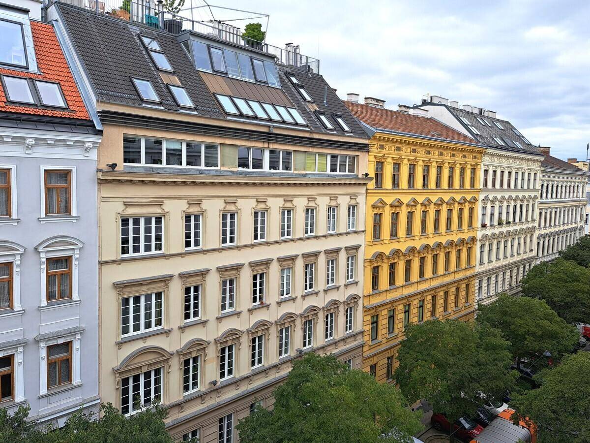 Historische Gebäudezeile mit farbigen Fassaden und Dachgauben unter einem bewölkten Himmel.