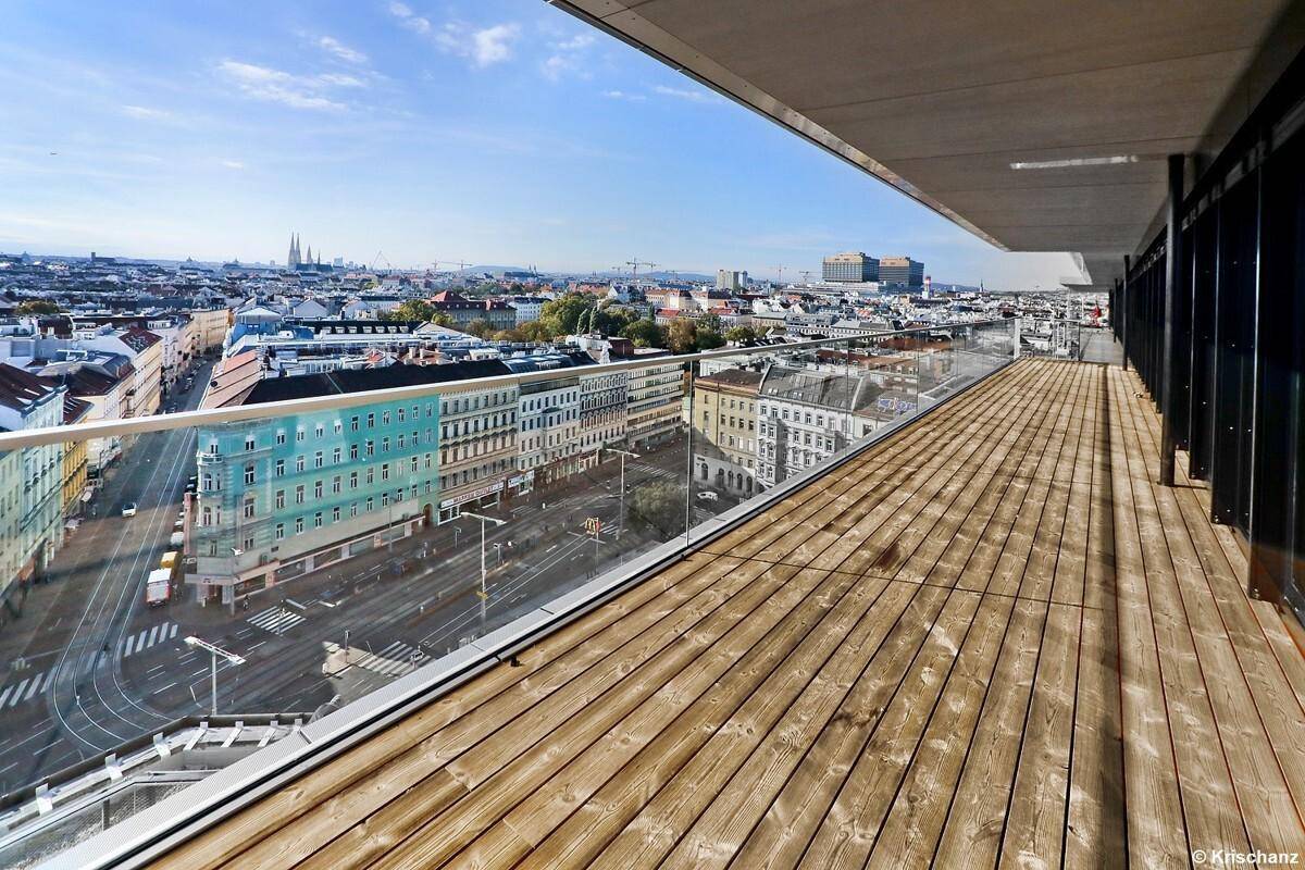Lange Terrasse mit Holzdielen und Glasbrüstung, die einen Panoramablick auf die städtische Umgebung ermöglicht.