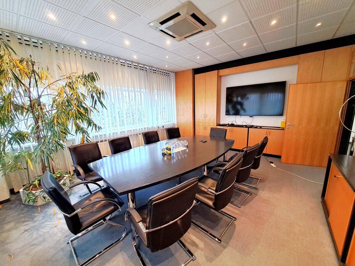 Eleganter Konferenzraum mit großem Holztisch, Ledersesseln und einem Flachbildschirm an der Wand.