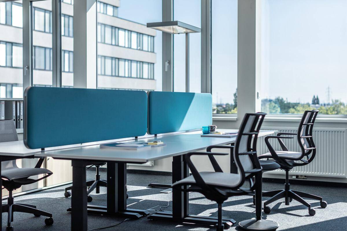 Heller Arbeitsplatz in einem modernen Büro mit großen Fenstern und ergonomischen Bürostühlen.