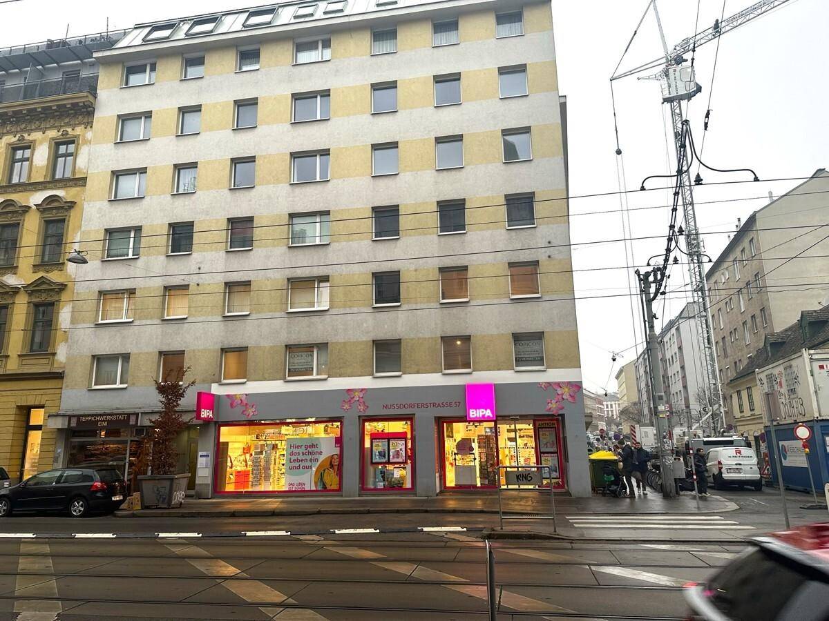 Mehrstöckiges Gebäude an einer Straßenecke mit Geschäften im Erdgeschoss und Wohnungen darüber.