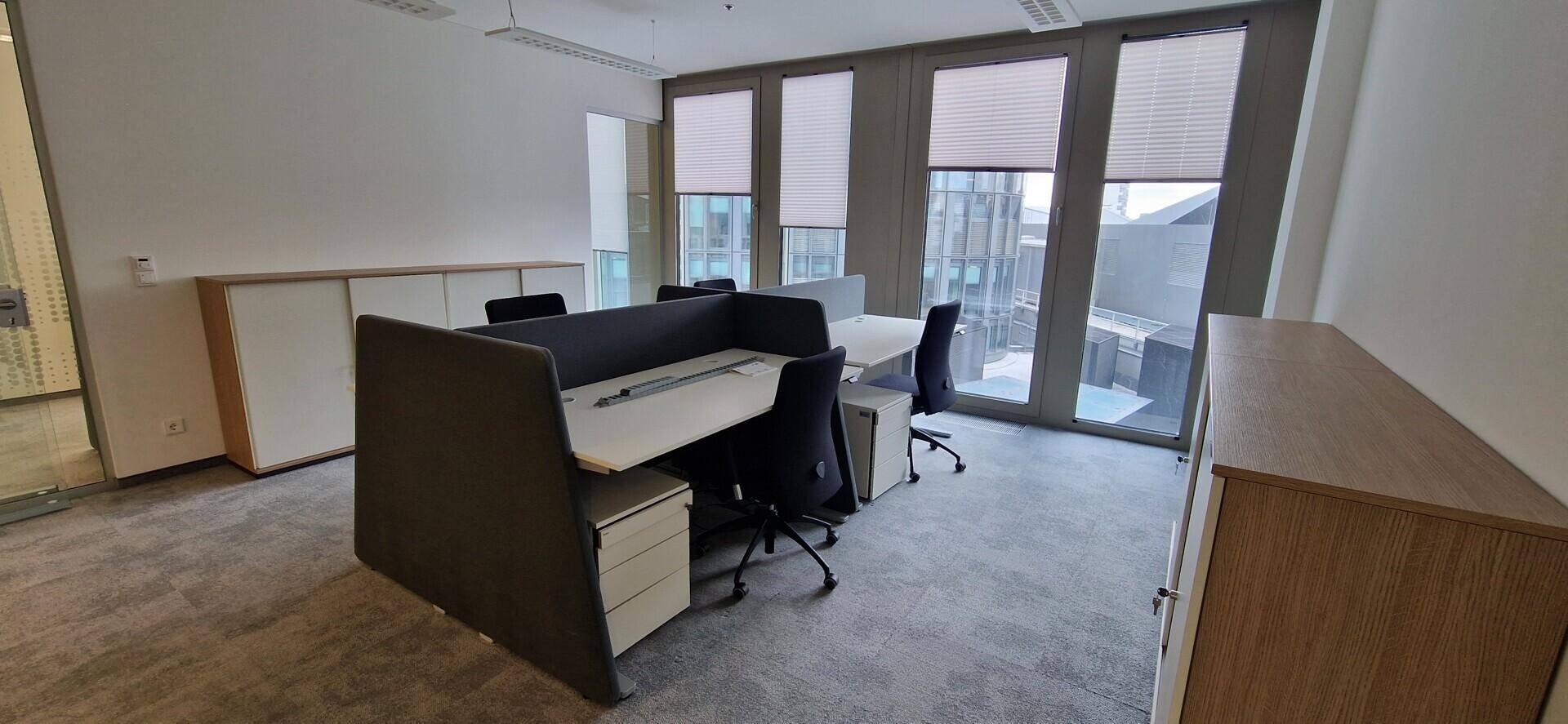 Moderner Büroraum mit ergonomischen Arbeitsplätzen, Teppichboden und großen Fenstern mit Blick nach draußen.