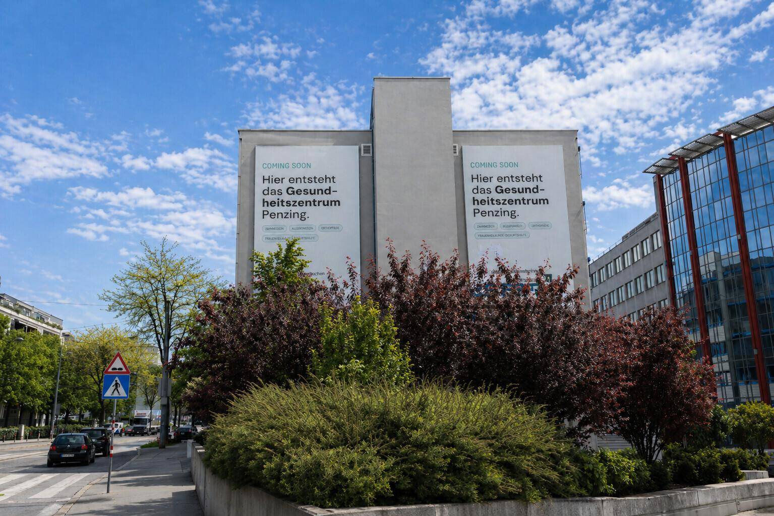 Vorderansicht des Gebäudes mit Werbebannern, umgeben von üppiger Bepflanzung.
