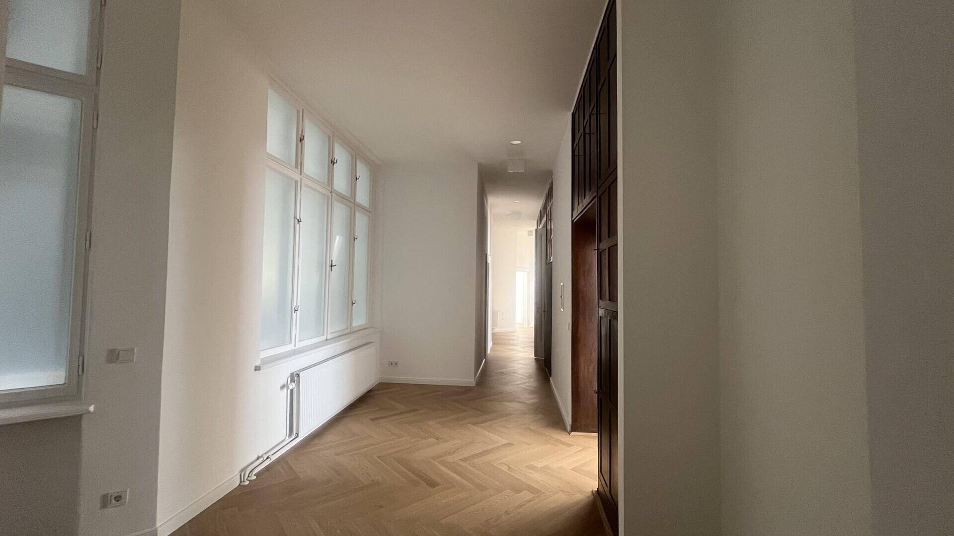Langer, heller Flur mit Fischgrätparkett und einer Reihe von Fenstern, die den Raum mit Licht füllen.